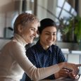 Caucasian short-haired woman contact with Indian colleague international department company staff members working together use laptop, take break use internet browse web have fun at workplace concept