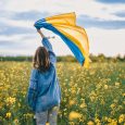 Ukrainian patriot woman waving national flag in canola yellow field. Rare, back view. Ukraine unbreakable, peace, independence, freedom, victory in war. High quality photo